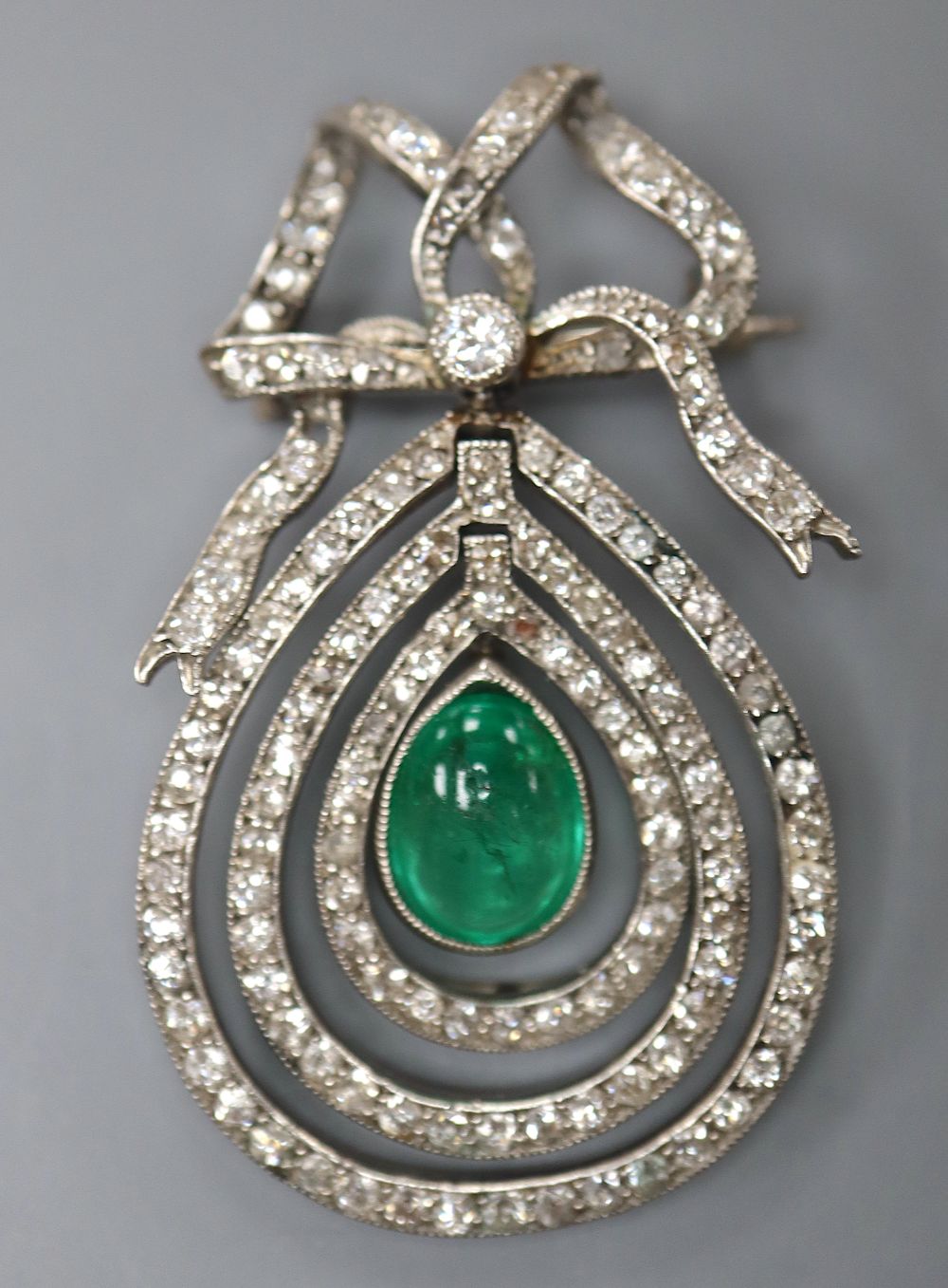 An Edwardian articulated white metal, cabochon emerald and diamond set teardrop shaped drop brooch,